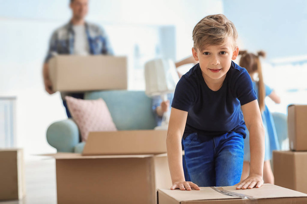 Χαριτωμένο παιδί με το κιβώτιο με την οικογένειά του συσκευασίας τα υπάρχοντά στο σπίτι. Μετακίνηση σε νέο σπίτι - Φωτογραφία, εικόνα