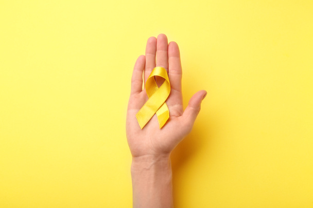 Female hand holding yellow ribbon on color background. Cancer concept - Foto, imagen