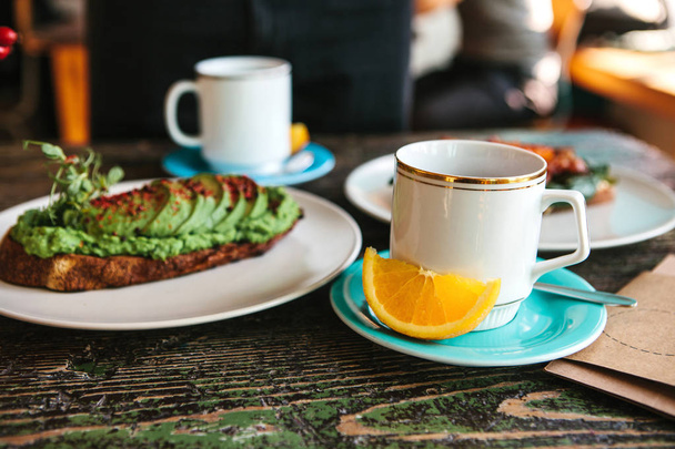 A cup of fresh fragrant tea and next to it a useful and nutritious sandwich with avocado lie on the table. Good morning breakfast - Foto, imagen