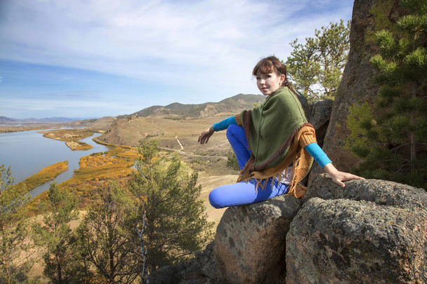 Nuori kaunis nainen poseeraa kalliolla vuorilla taustalla joen ja laakson alla
. - Valokuva, kuva