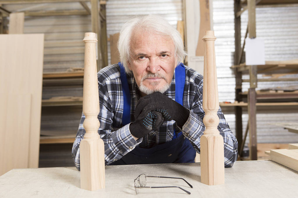 Serious diseñador de muebles cuidadosamente pule el marco de la silla, que está ocupado fabricando en su taller de carpintería, con estantes de objetos de madera y patrones detrás de él
 - Foto, Imagen