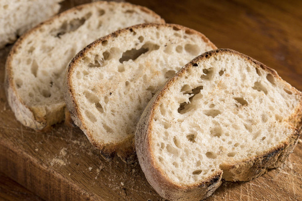 Freshly sliced sliced panini bread on a wooden cutting board in soft window light - Zdjęcie, obraz