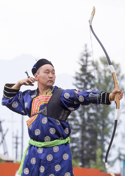 Competiciones en tiro desde un arco deportivo en Siberia. Mongolia competiciones en tiro con arco. El deportista está vestido con un traje tradicional de Buryat-Mongolia, disparando con sus flechas durante una fiesta nacional
. - Foto, imagen