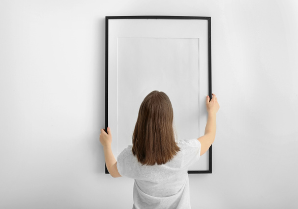 Mujer colgando marco de fotos en blanco en la pared blanca
 - Foto, Imagen