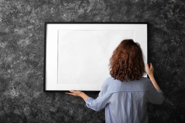 Woman hanging blank photo frame on dark wall - Фото, изображение