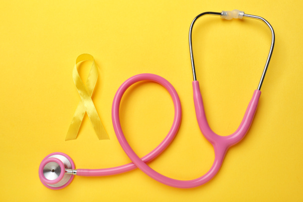 Yellow ribbon and stethoscope on color background. Cancer concept - Photo, Image