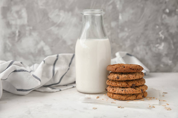 Deliziosi biscotti di farina d'avena e bottiglia di latte sul tavolo su sfondo grigio
 - Foto, immagini