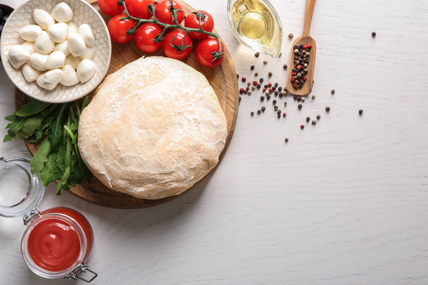 Composition with raw dough and ingredients for pizza on light background - Photo, image