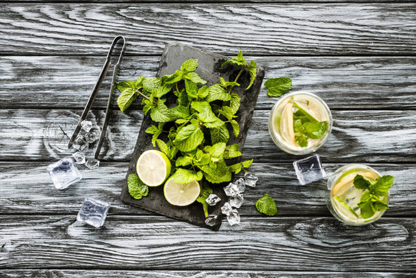 top view of mint, lime, ice cubes and glasses with mojito on wooden surface - Photo, Image