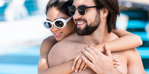 beautiful couple in sunglasses embracing near swimming pool - Foto, Bild