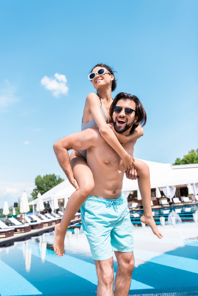 handsome man piggybacking his girlfriend near swimming pool - Фото, зображення