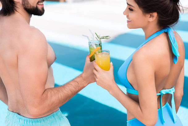 young couple clinking with glasses of alcohol cocktails near swimming pool - Foto, afbeelding
