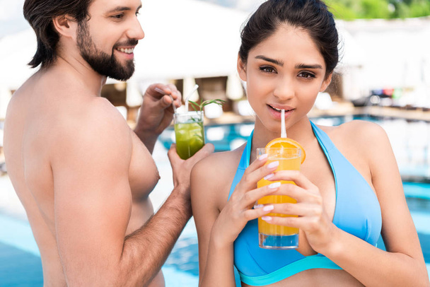 young couple drinking fresh cocktails near swimming pool - Фото, изображение