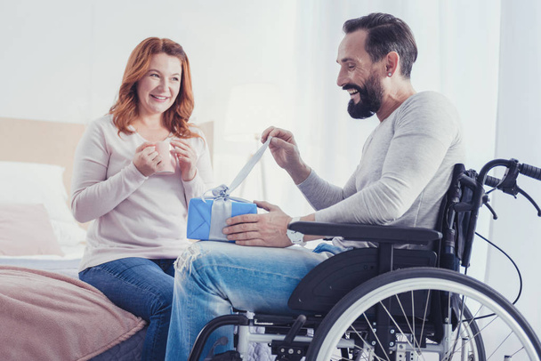 Happy man sitting in his wheelchair and opening a beautiful present - Φωτογραφία, εικόνα