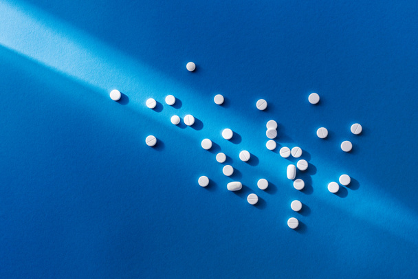 elevated view of white tablets on blue background with sunlight - Φωτογραφία, εικόνα