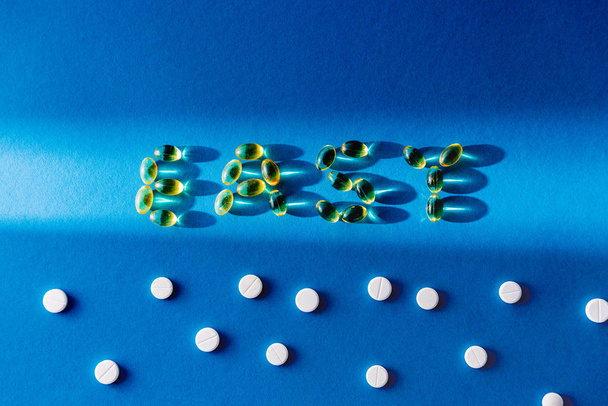 top view of lettering easy by pills near white tablets on blue background with sunlight  - Fotó, kép