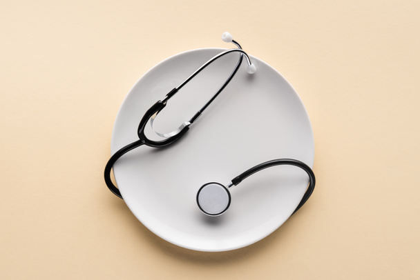 top view of plate wrapped by stethoscope on beige background  - Фото, зображення
