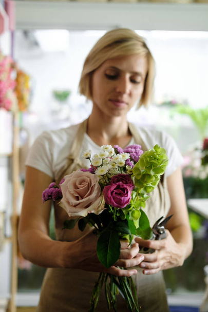 γυναίκα ανθοκόμος κάνει εσωτερική μπουκέτο με ροζ λουλούδια. Θηλυκό ανθοπωλείο προετοιμασία μπουκέτο με τριαντάφυλλα σε ανθοπωλείο. επιχειρηματικότητας, μικρή επιχείρηση, έννοια στον χώρο εργασίας  - Φωτογραφία, εικόνα