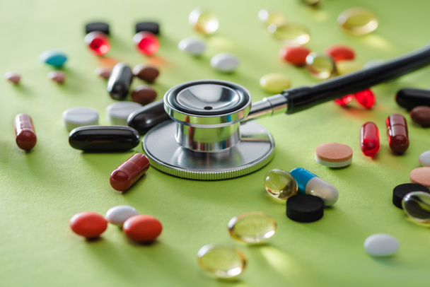 selective focus of stethoscope surrounded by various pills on green surface  - Photo, Image