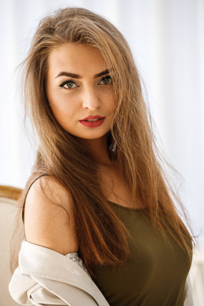 Fashion studio shot of beauty female model sitting on wooden chair in luxury apartments. Young woman with professional makeup wearing casual clothes in hotel interior. - Fotografie, Obrázek
