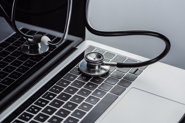 selectieve aandacht van stethoscoop en laptop met leeg scherm op grijze oppervlak  - Foto, afbeelding
