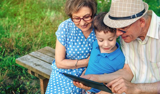 Бабушка с дедушкой и внук сидят на скамейке на планшете
 - Фото, изображение