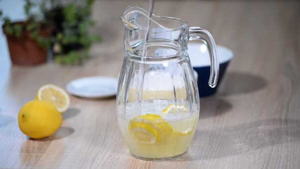 En una jarra de limones vierte agua. Vaso de soda de agua con gas bebida limonada con hielo y limón rodaja sobre fondo blanco
. - Imágenes, Vídeo