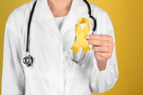Doctor with yellow ribbon on color background, closeup. Cancer awareness concept - Photo, Image