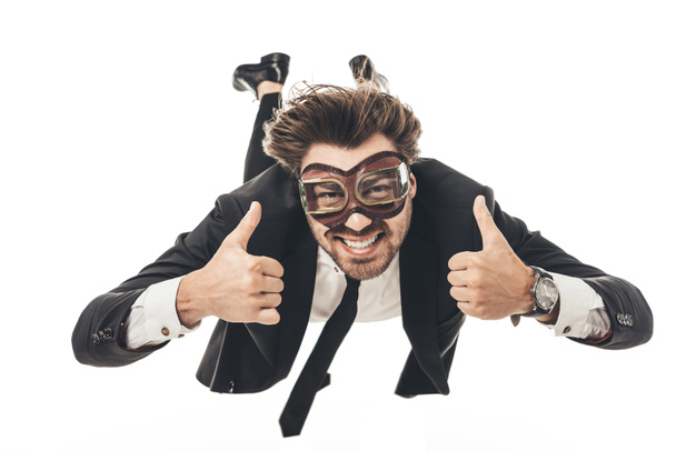 Lächelnder junger Geschäftsmann mit Oldtimer-Fliegerbrille fällt und zeigt vereinzelt Daumen hoch auf weiß - Foto, Bild