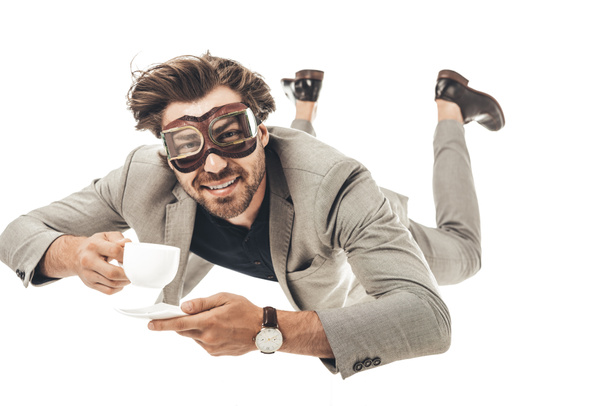 handsome young businessman in vintage aviation goggles falling with cup of coffee isolated on white - Fotografie, Obrázek