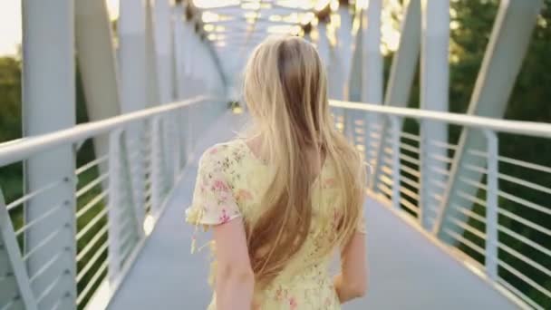 Uma mulher a olhar para trás na ponte. Mulher loira bonita olhando para a câmera enquanto corria na ponte com cabelo ondulado. - Filmagem, Vídeo
