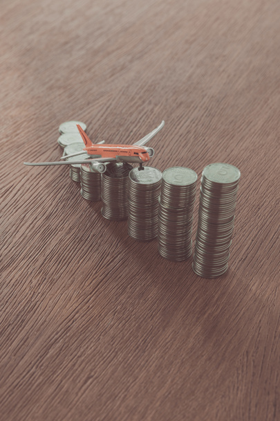 toy plane on stacks of coins on wooden tabletop, saving concept - Photo, Image