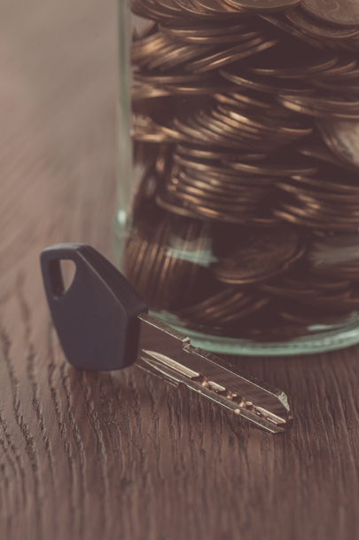 key near jar of coins on wooden tabletop, saving concept - Photo, Image