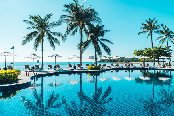 Krásná tropická pláž a moře s deštníkem a židlí kolem bazénu v hotelovém resortu pro cestování a dovolenou - Fotografie, Obrázek