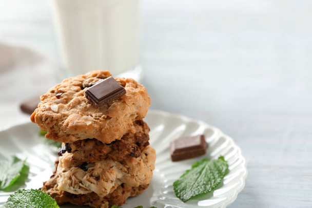 Plate with tasty oatmeal cookies, chocolate and mint leaves on table - Photo, Image