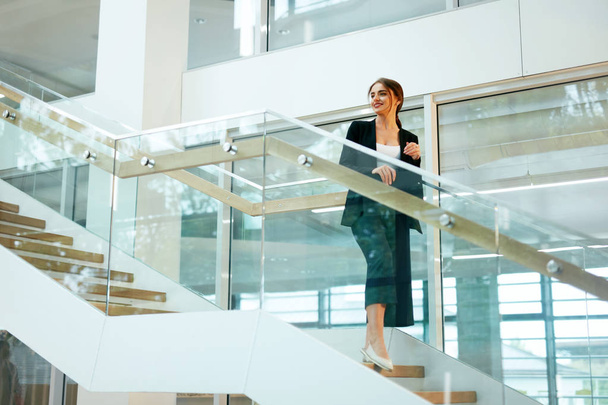 Business Woman In Office Interior. Female Worker With Folder On Stairs In Modern Office Building. High Resolution - 写真・画像