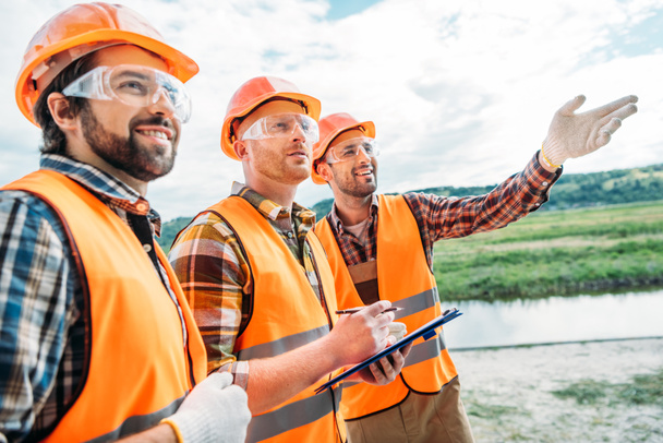 group of builders in hard hats and reflective vests pointing somewhere - Фото, изображение