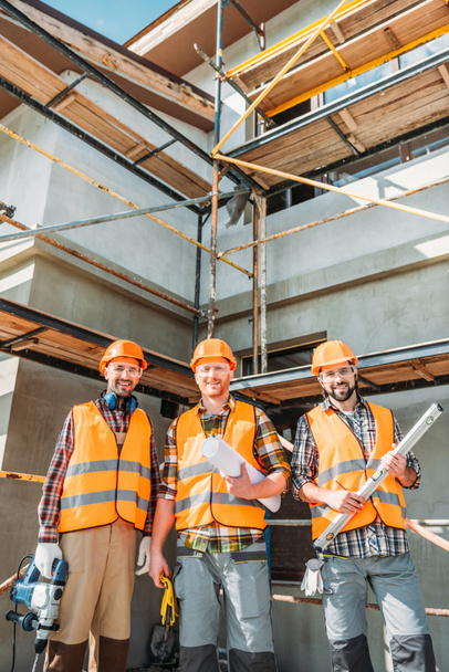 Gruppe lächelnder Bauarbeiter blickt auf Baustelle in die Kamera - Foto, Bild