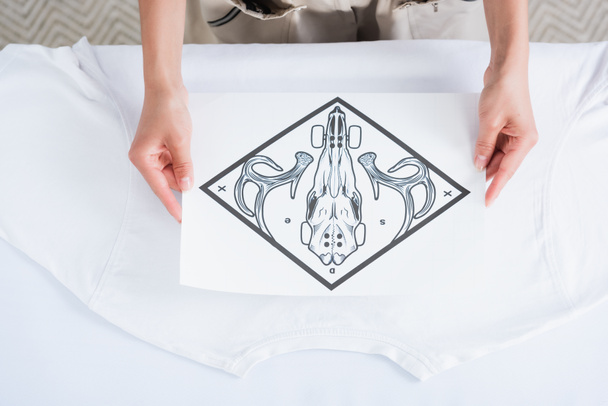 обрезанное изображение женщины-модельера, выбирающей печать для пустой белой футболки
  - Фото, изображение