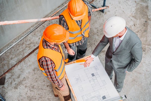 high angle view of builders and architect discussing blueprint at construction site - Photo, Image