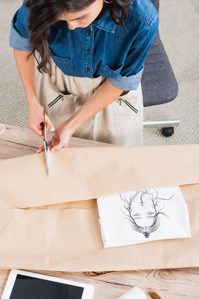 κάτοψη της γυναικείας σχεδιαστής μόδας περιτυλίγματος t-shirt με εκτύπωση σε χαρτί το πακέτο στο τραπέζι - Φωτογραφία, εικόνα