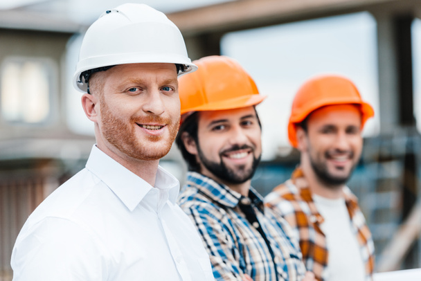 group of smiling architects in hard hats looking at camera - Photo, Image