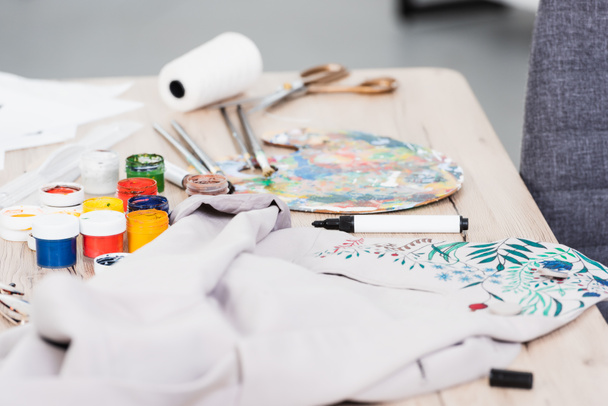 selective focus of colorful paints and painting jacket at table in clothing design studio  - Photo, Image