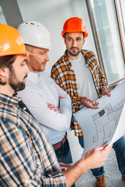 group of architects with blueprint having conversation inside of constructing building - Photo, Image