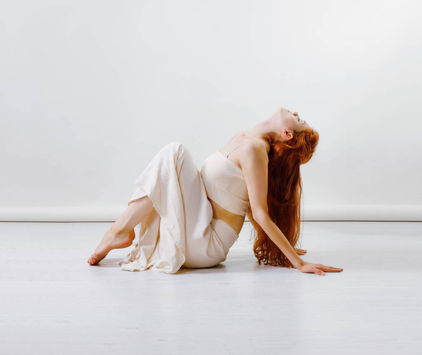 コンテンポ ラリー ダンスを踊り、スタジオでポーズをとって、床に座っての若い赤毛の女性。コピー スペース - 写真・画像