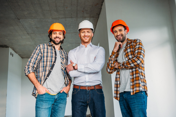 group of smiling architects inside of constructing building looking at camera - Foto, imagen