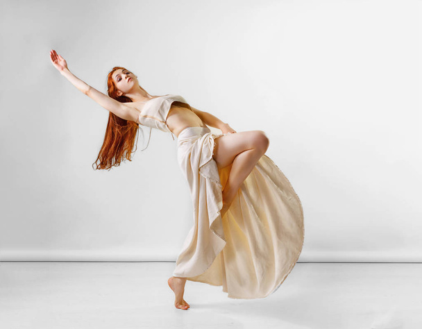 Bailarina posando en el estudio. Chica pelirroja joven y hermosa en una falda larga beige y top baila y posa en el estudio. Copiar espacio
 - Foto, Imagen