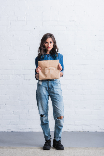 attractive young woman holding paper package in front of brick wall  - Photo, Image