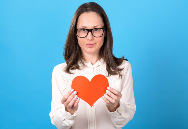 Young woman in glasses holds a red heart in her hands as a symbol of health. In the meaning of love. - Photo, image