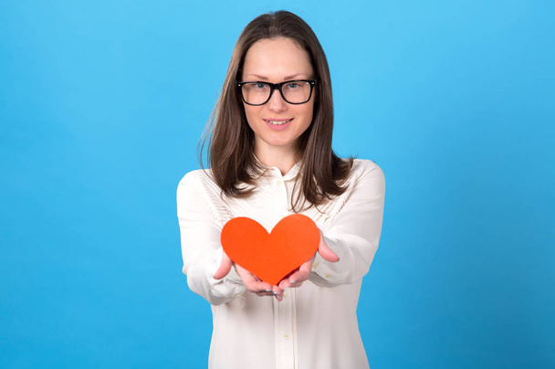 Young woman in glasses holds a red heart in her hands as a symbol of health. In the meaning of love. - Photo, image